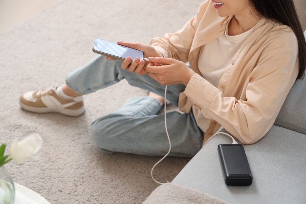 Frau nutzt Powerbank um Smartphone zu laden – digitale Hilfe im Notfall mit Schluesseldienst Neuss