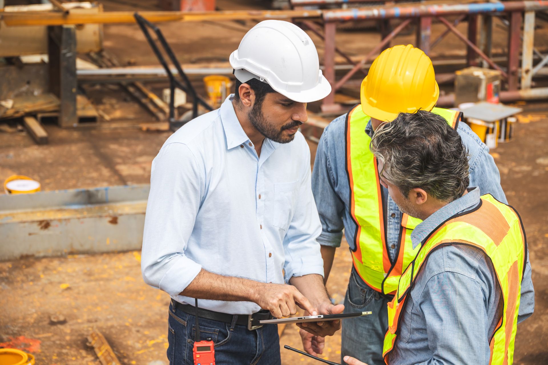 Gruppe von Bauarbeitern mit Schutzhelmen und Warnwesten spricht ueber Sicherheit auf der Baustelle und dokumentiert Arbeitsschutzmassnahmen