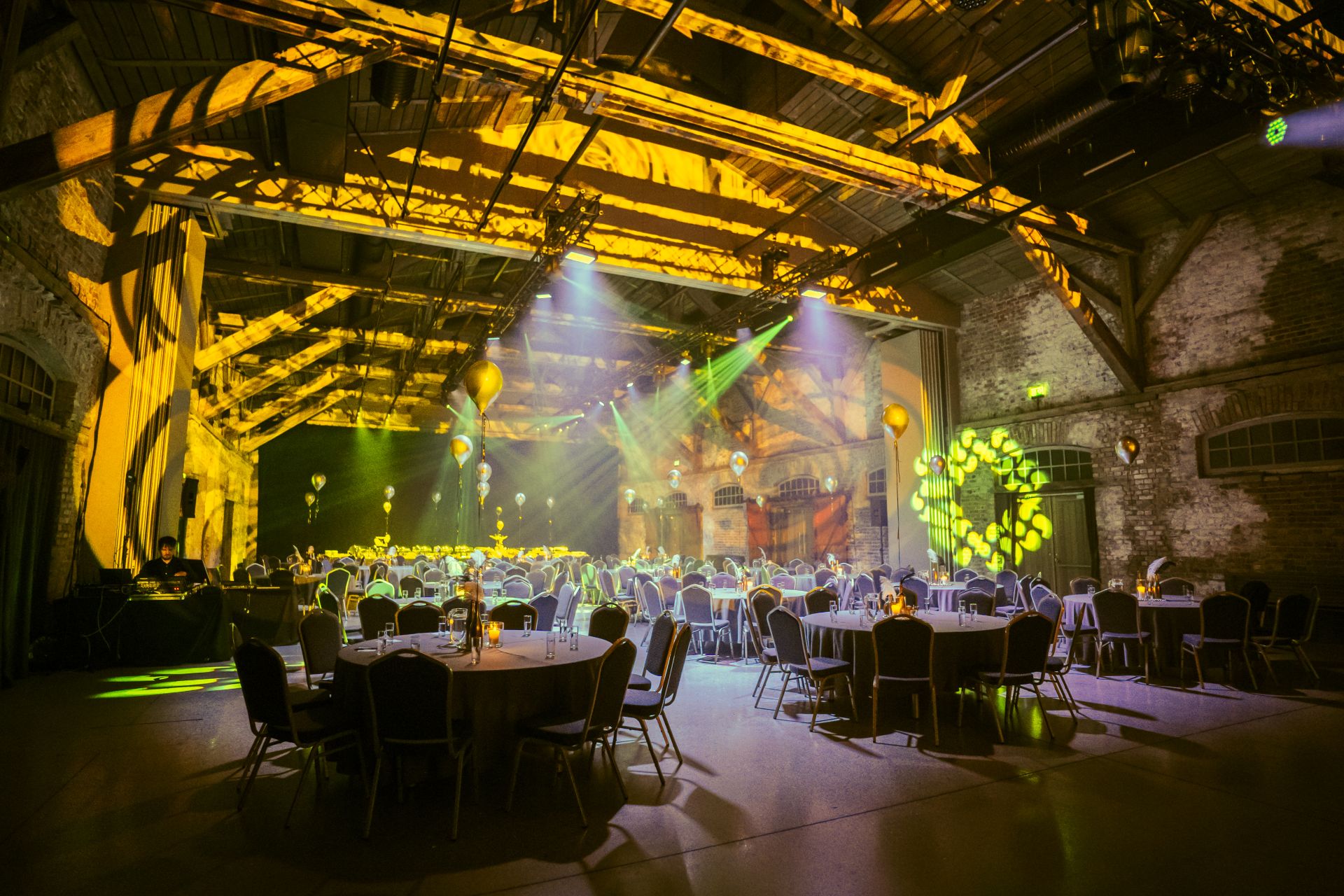 Eventlocation in industrieller Halle mit runden gedeckten Tischen, atmosphaerischer Lichtinstallation und festlicher Bestuhlung