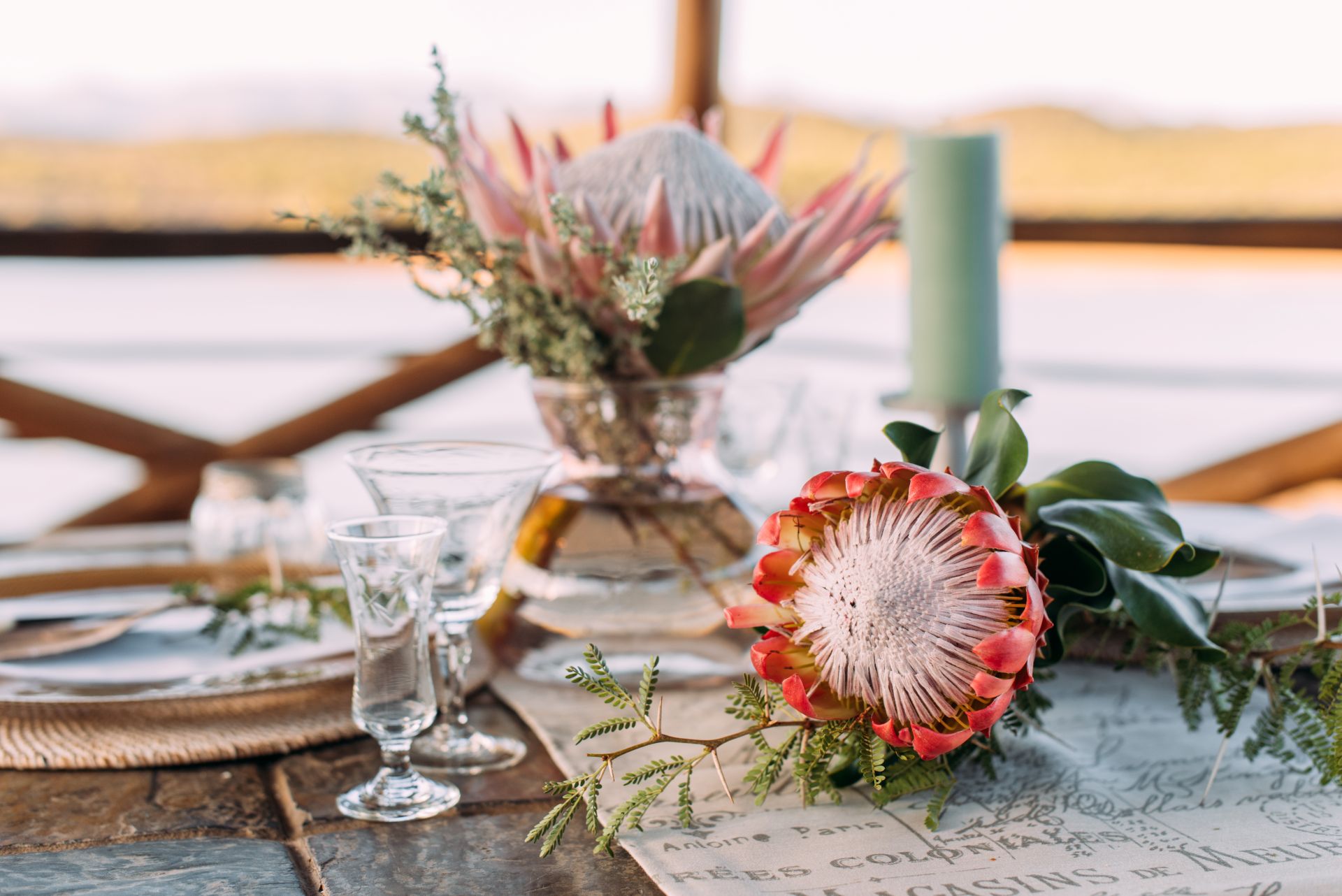 Nahaufnahme einer Tischdekoration mit Protea-Blumen, Glasglaesern und natuerlichen Arrangements